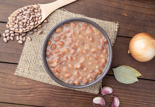 Cooked brown beans in a bowl over wooden table with onion and garlic.